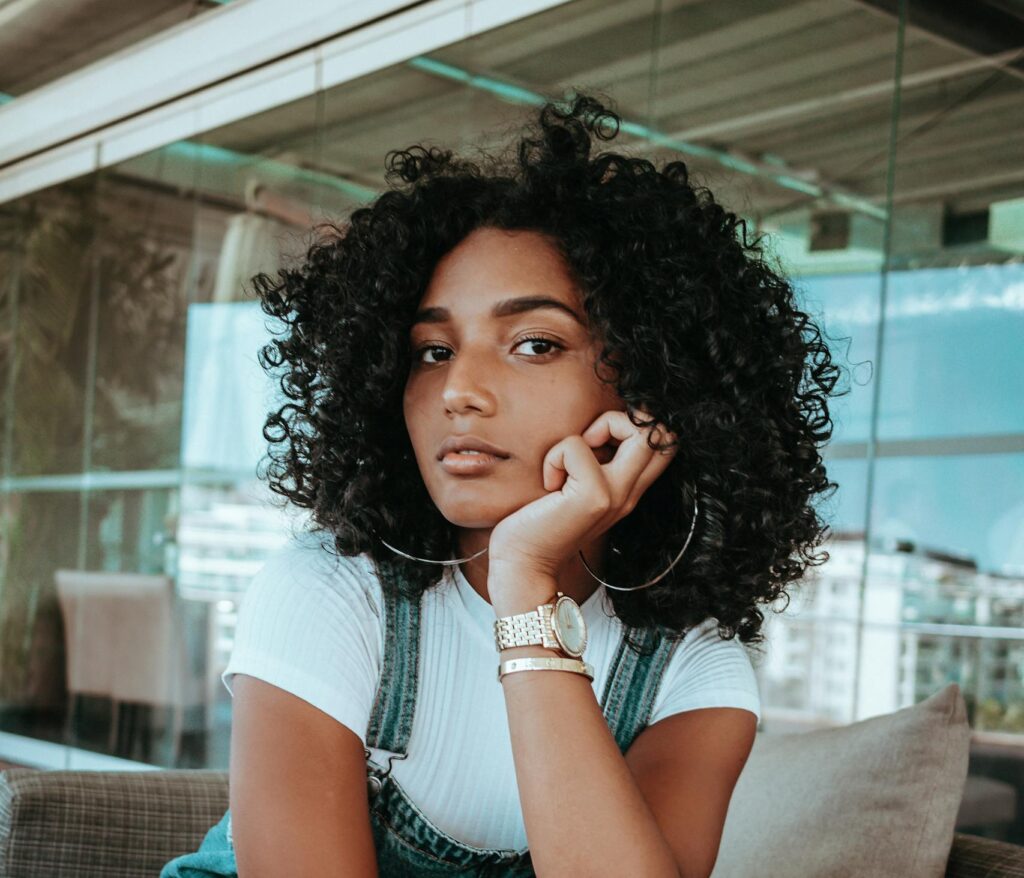 Woman with Curly Black Hair Kneeling on Sofa with Head Propped Up