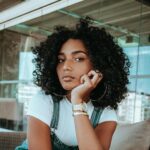 Woman with Curly Black Hair Kneeling on Sofa with Head Propped Up